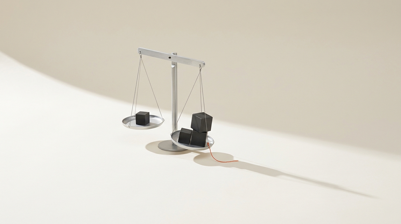A precision laboratory balance on a bone-coloured surface with one pan tipped lower under two stacked graphite cubes and an orange thread tied to the suspension wire.